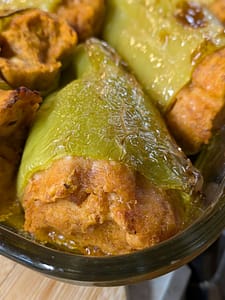Baked stuffed cubanelle peppers in a baking dish with golden bread stuffing peeking out.