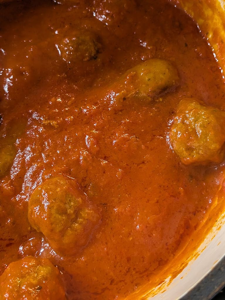 Homemade meatballs and Italian sausage simmering in marinara sauce for lasagna, rich with herbs and slow-cooked flavor