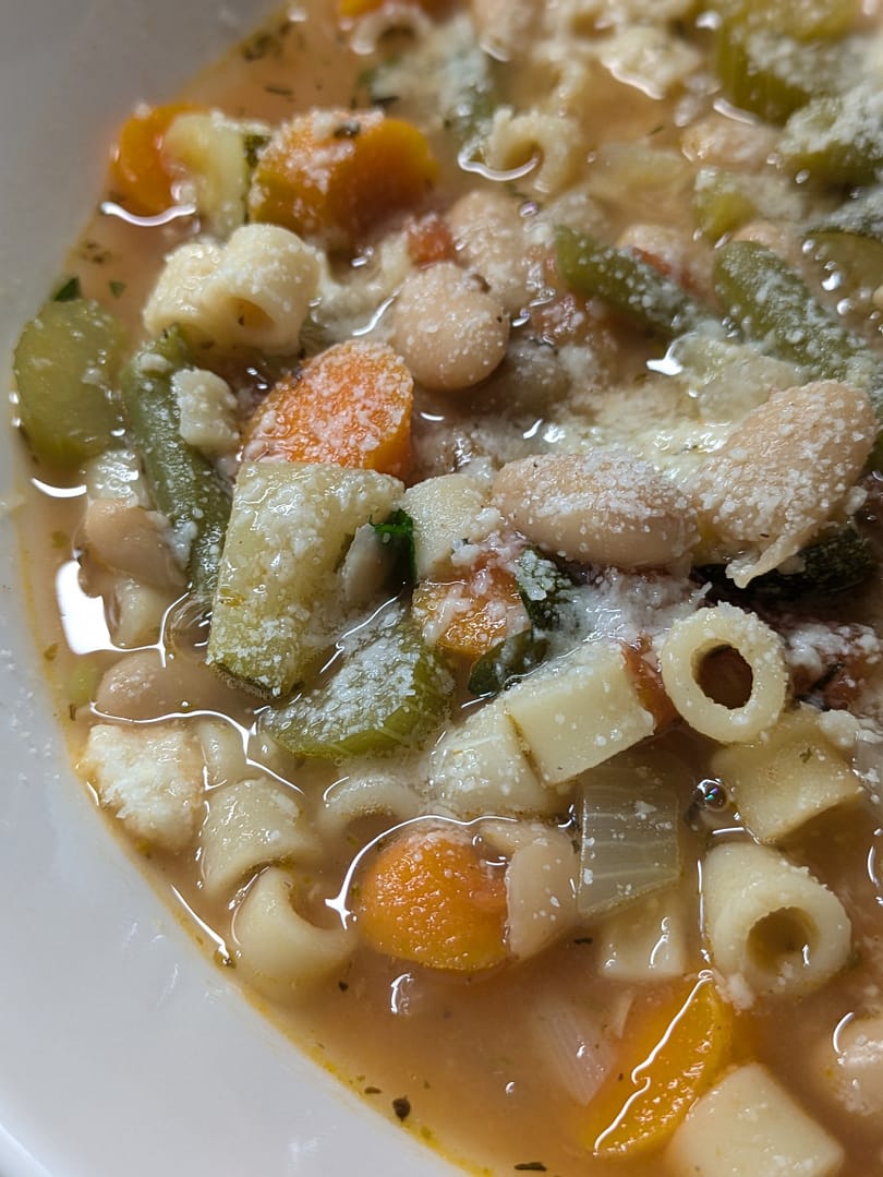 Bowl of homemade minestrone soup filled with ditalini pasta, white beans, carrots, celery, zucchini, and green beans in a savory vegetable broth, topped with grated Parmesan