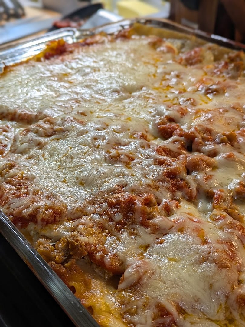 Homemade meatball and sausage lasagna layered with ricotta, marinara sauce, and melted mozzarella, served hot and cheesy from a glass baking dish