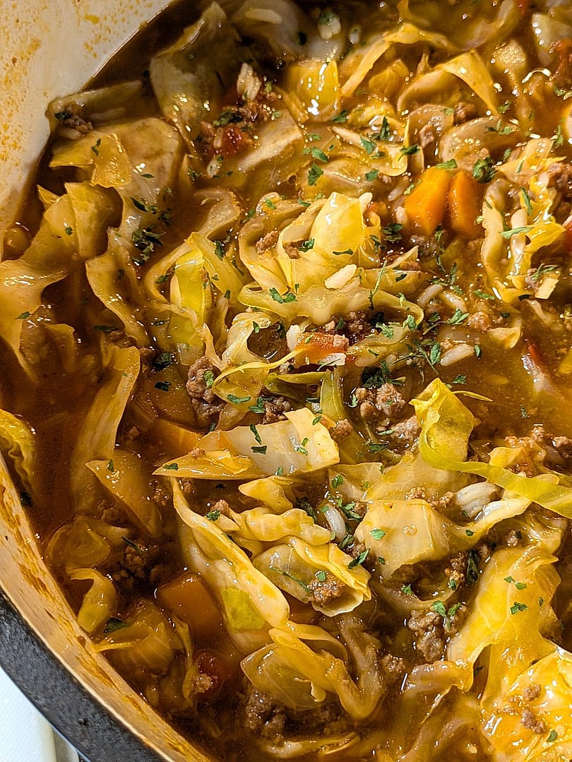Hearty unstuffed cabbage roll soup simmering in a Dutch oven with ground beef, cabbage, carrots, and tomato broth, topped with chopped parsley