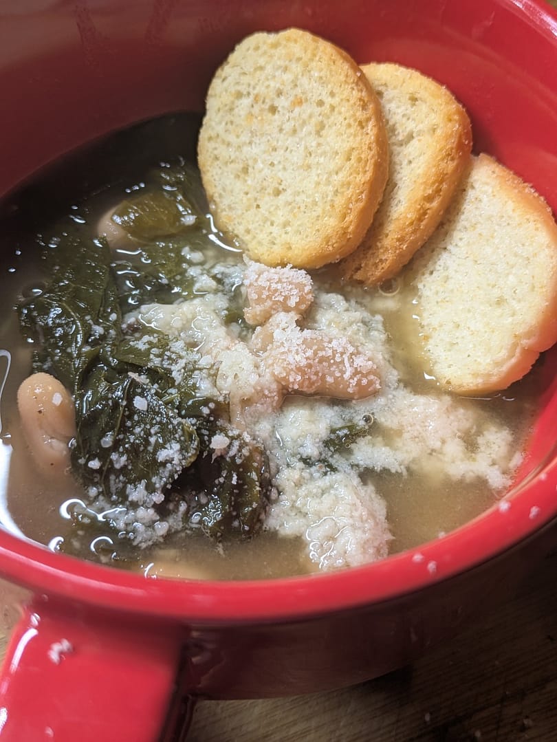Bowl of escarole and bean soup topped with parmesan and served with crusty bread