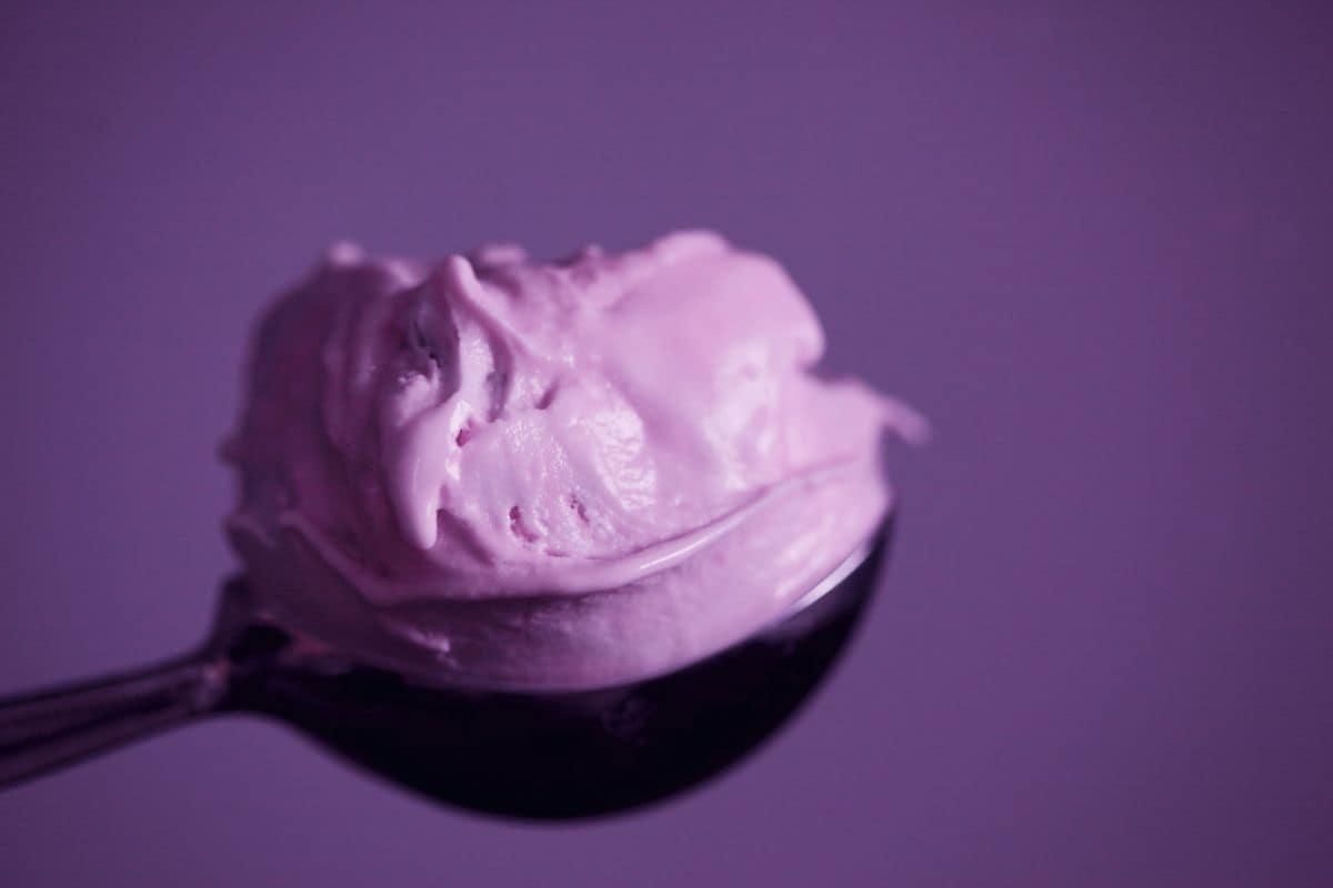 Close-up of a spoon holding a scoop of creamy purple ice cream, set against a matching purple background.