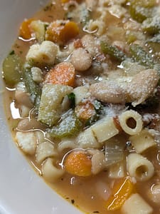 Bowl of homemade minestrone soup filled with ditalini pasta, white beans, carrots, celery, zucchini, and green beans in a savory vegetable broth, topped with grated Parmesan