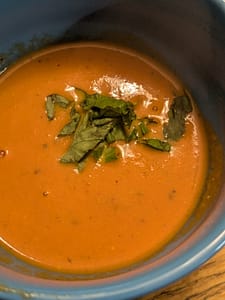 Close-up of creamy tomato basil soup with swirls of heavy cream and fresh basil ribbons.