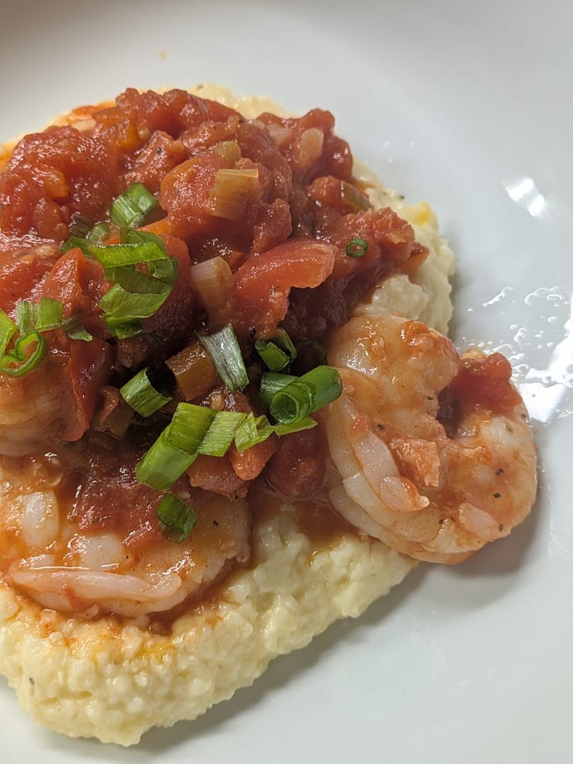 Southern-style shrimp and grits topped with tomato-based Creole sauce and sliced green onions, served on a white plate for a cozy, comforting meal